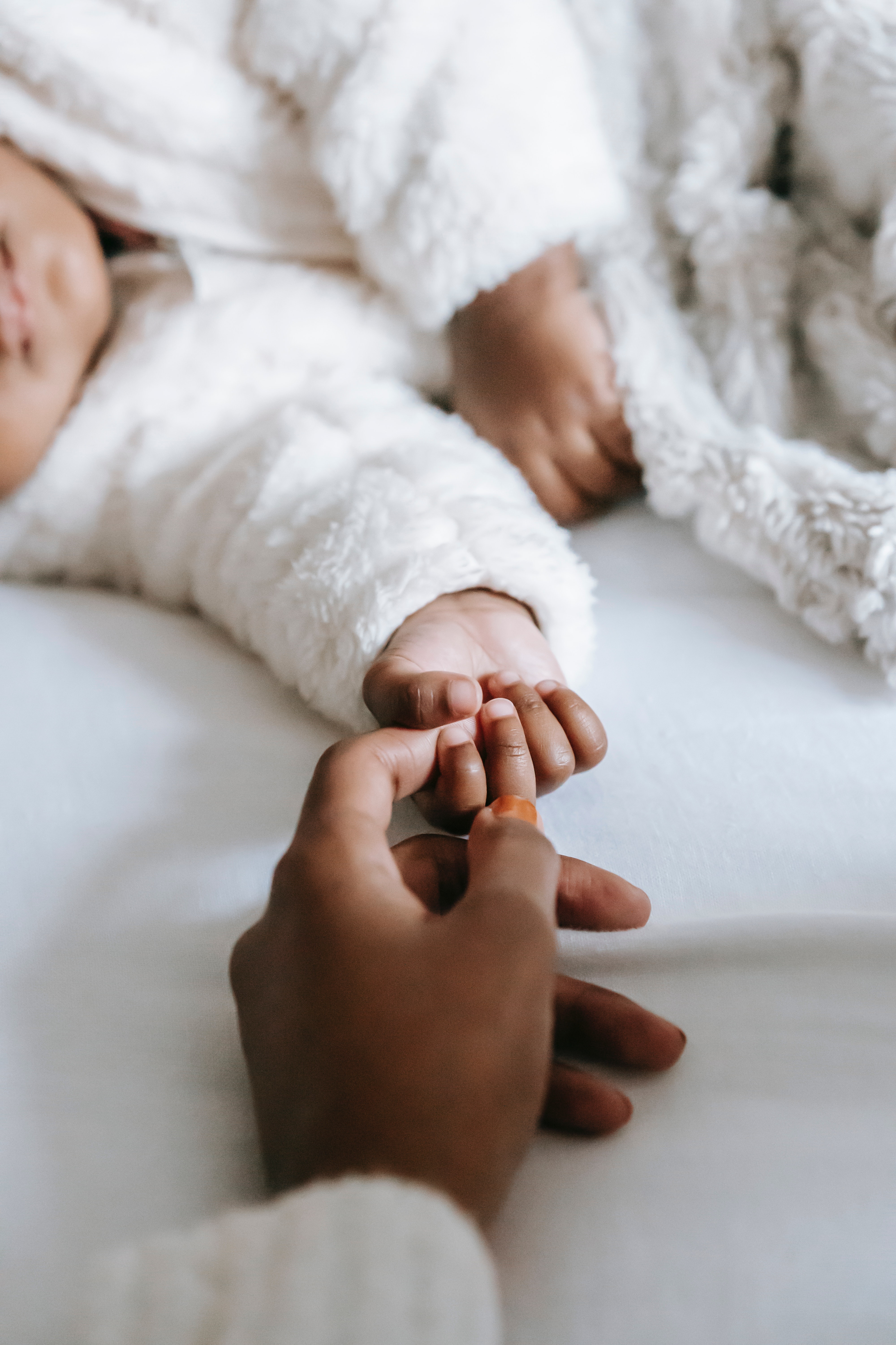 Closeup of parent's hand holding hand of sleeping baby.