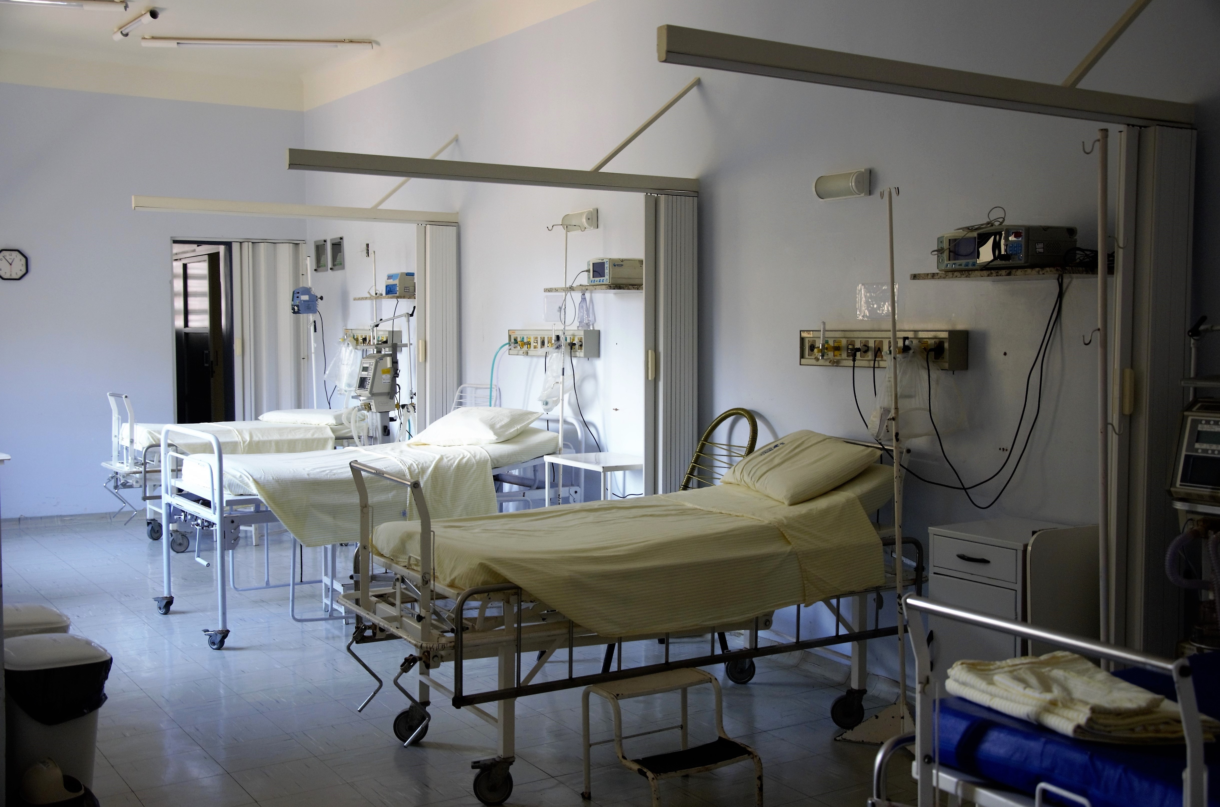 Empty hospital beds lined against a white wall with clean sheets and pillows.