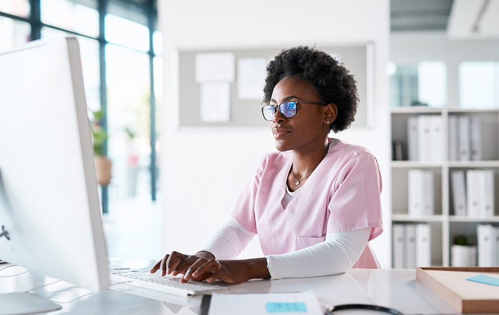 Bright image of an African American female nurse typing on the computer at a healthcare practice.