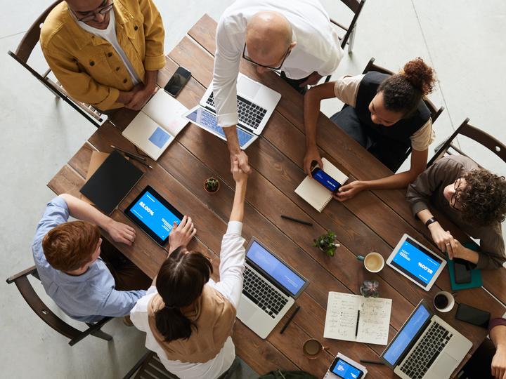 Overhead of employees shaking hands across a desk.