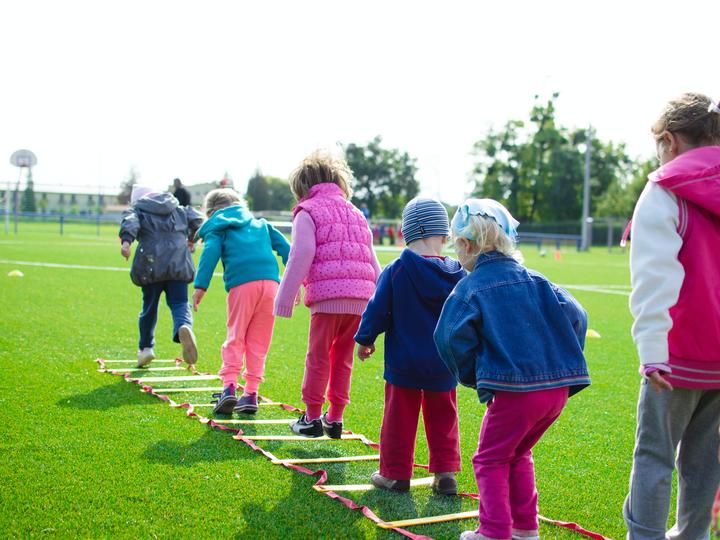 Children in bright colored jackets playing on grass outside.