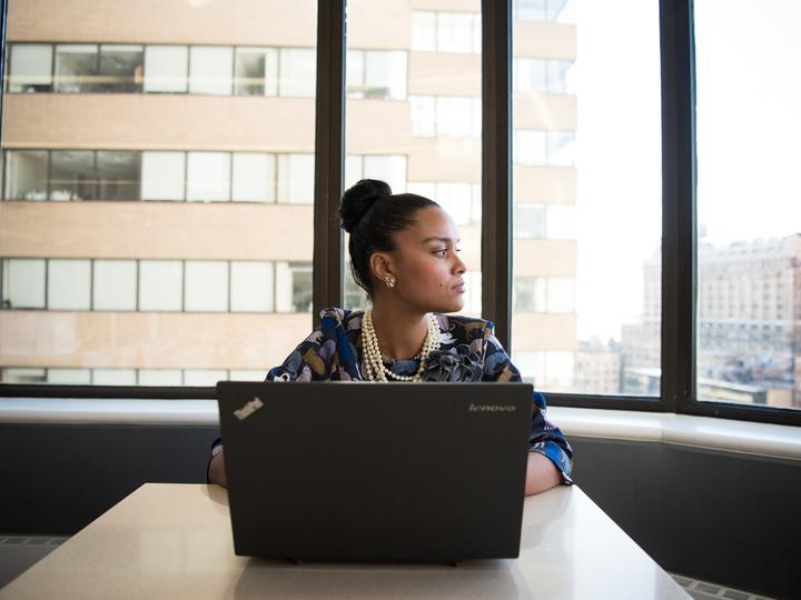 Businesswoman sitting in front of laptop computer looking out of office window.