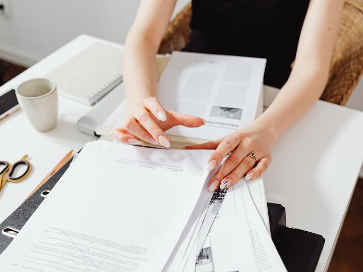 Woman's hands going through stacks of papers on a white desk.