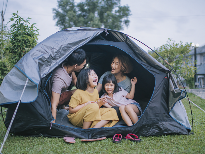 Asian family laughing inside camping tent in backyard of their house staycation weekend activities.