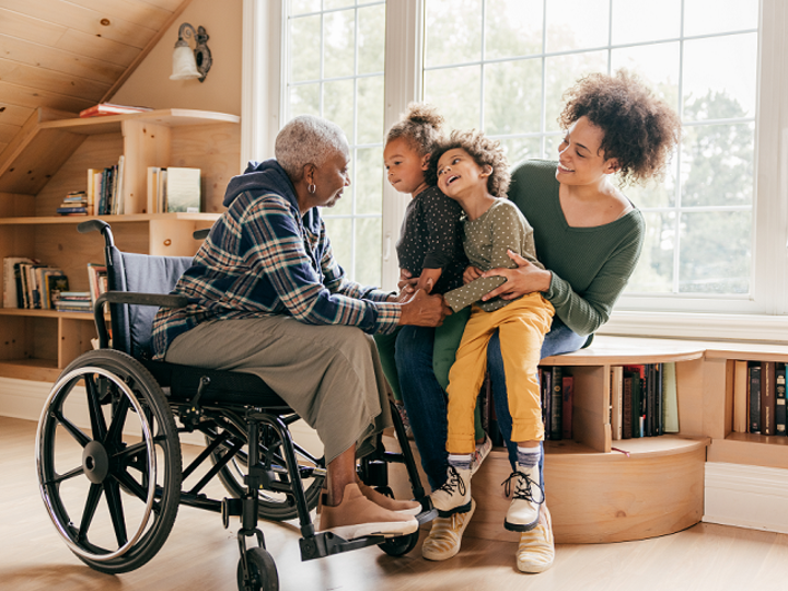 Grandson and grandmother in wheelchair holding hands during conversation with mom and sister.
