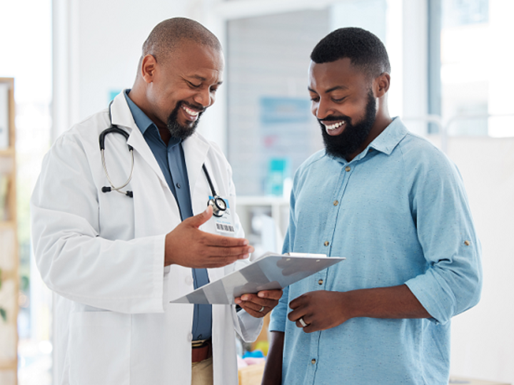 Elder African American doctor showing a young African American patient their results on a clipboard.