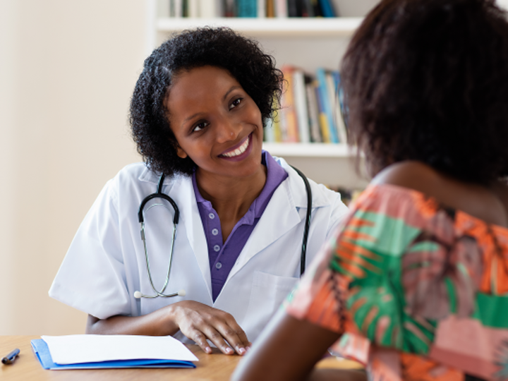Laughing African American female doctor with patient at hospital.