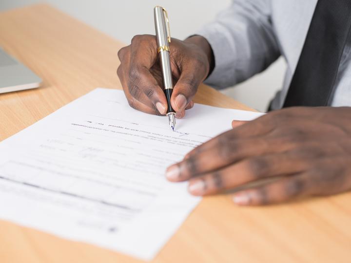 Closeup image of an African American man signing a document.
