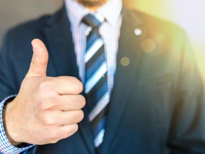 Closeup image of a caucasian man in a suit giving a thumbs up toward the camera.