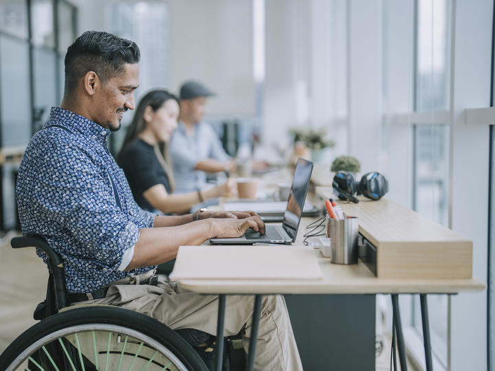 Male employee in wheelchair sitting at desk working on laptop