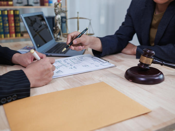 Hands of attorney and clients sitting at table with laptop and gavel , reviewing documents