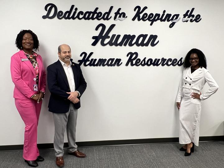 Three employees standing, posing in front of human resources sign 