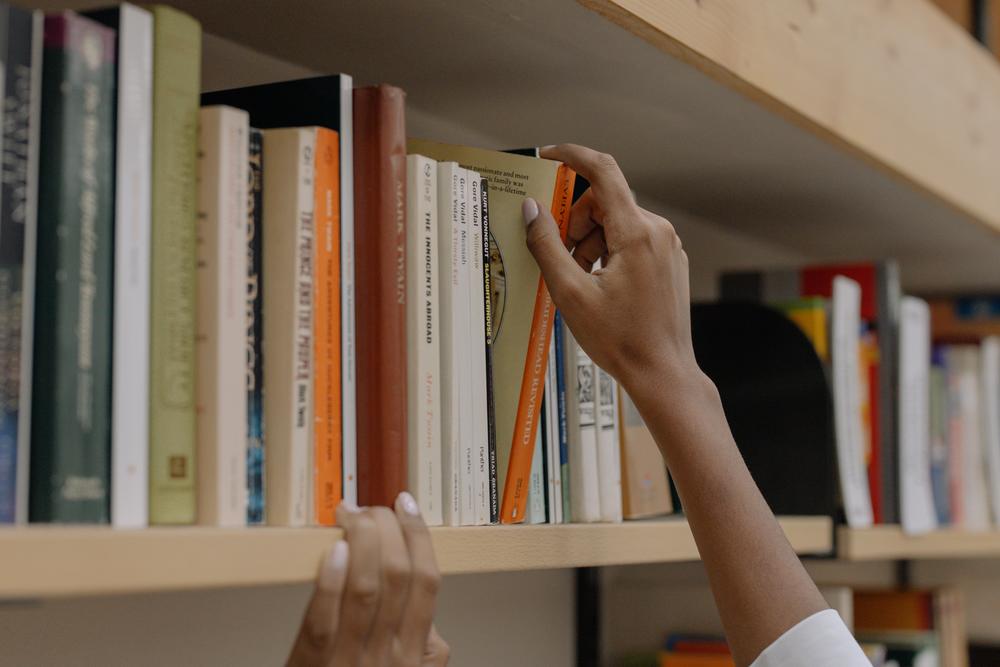 A woman's right hand reaches to pull a book from a library shelf.