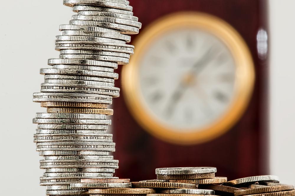 A blurry clock sits on the wall behind a stack of close-up coins.
