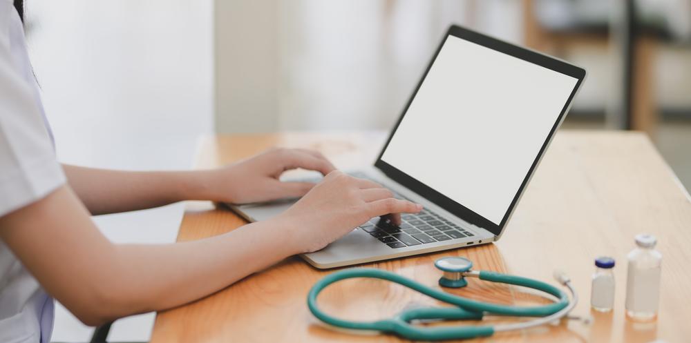 Person on laptop with green stethoscope and bottles on table.