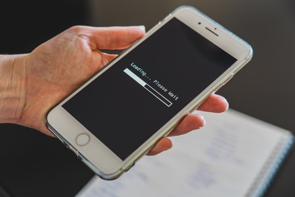 Hand holding cell phone with "loading... please wait" on screen.
