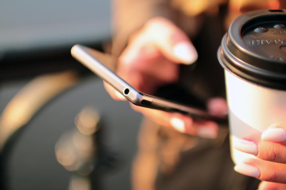 Person holding cell phone and cup.