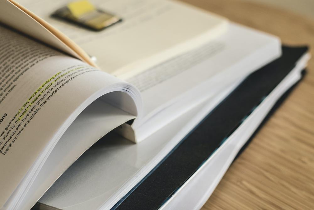 Folder, papers, open book and binder on a table.