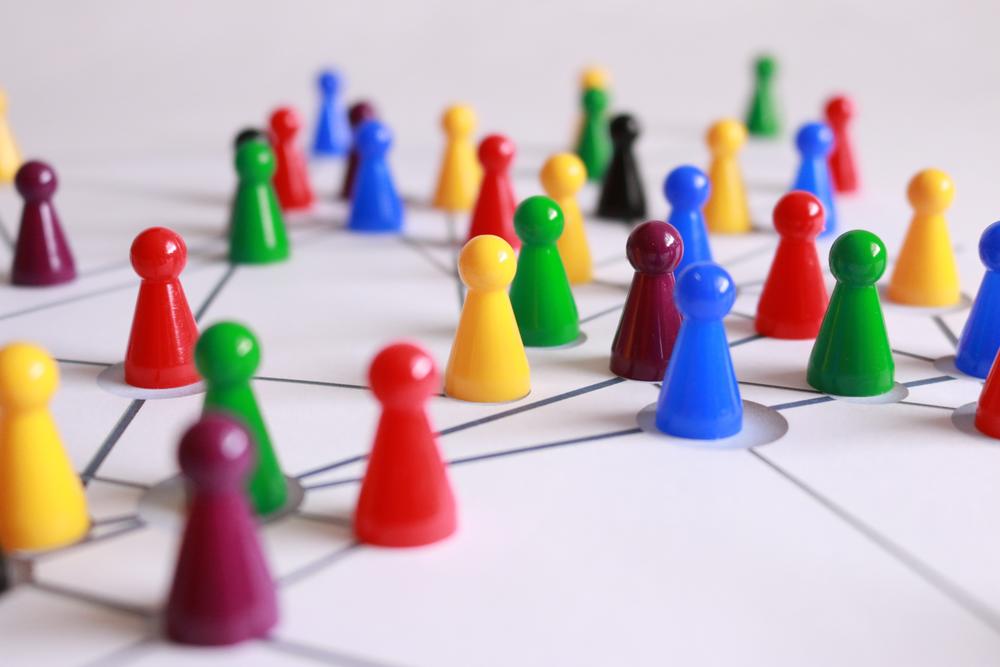 Colorful game pegs that are shaped like people arranged on a paper with lines connecting them, symbolic of strategy.