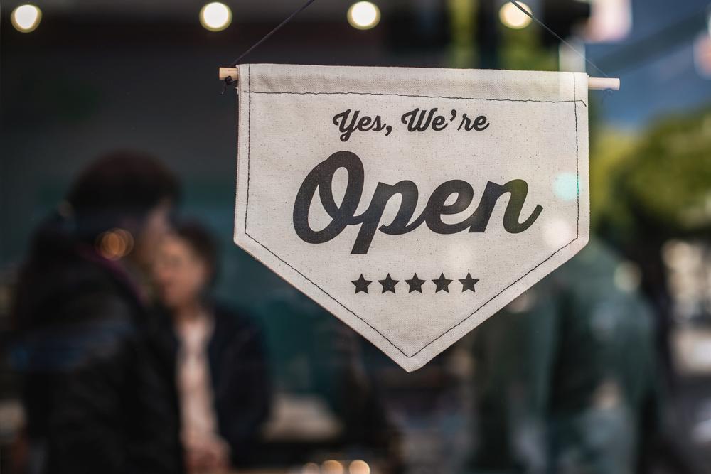 Closeup of pointed cloth sign saying "yes, we're open" on the door of a small business.