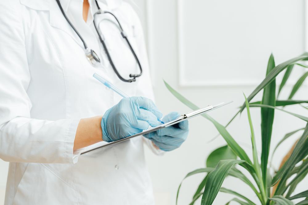 Doctor or nurse wearing stethoscope and gloves writing on clipboard.