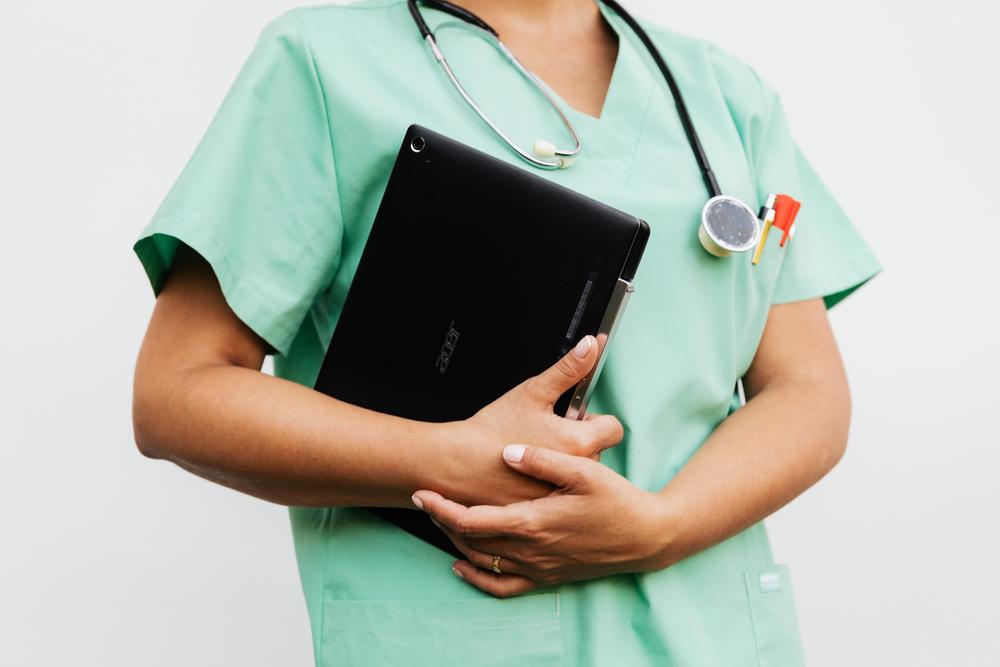 Nurse holding tablet wearing stethoscope and scrubs.