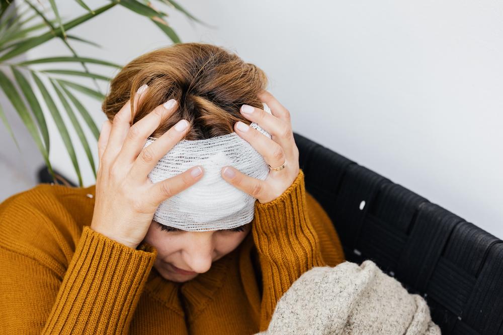 Woman in orange sweater holding bandaged head.