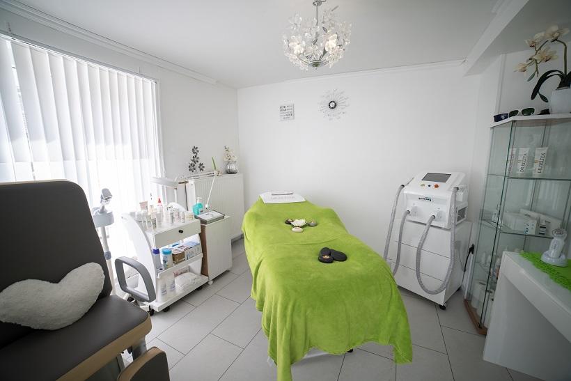 Inside of a health care facility office with patients table covered in green blanket between a machine and supplies.