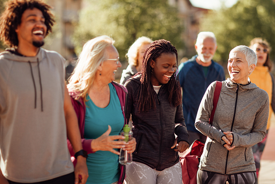 Active group of diverse adults and seniors laughing and walking in a park.