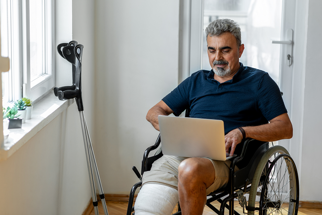 Senior man with broken leg on wheelchair at home.