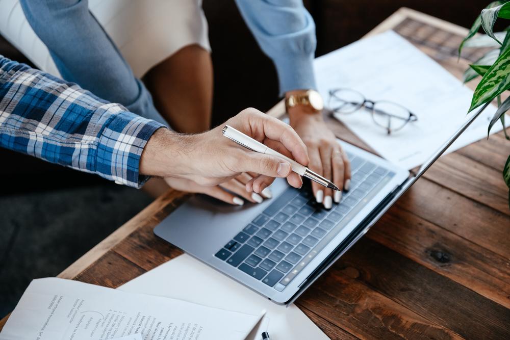 Two people over a laptop computer. One person pointing with pen, and the other person typing.