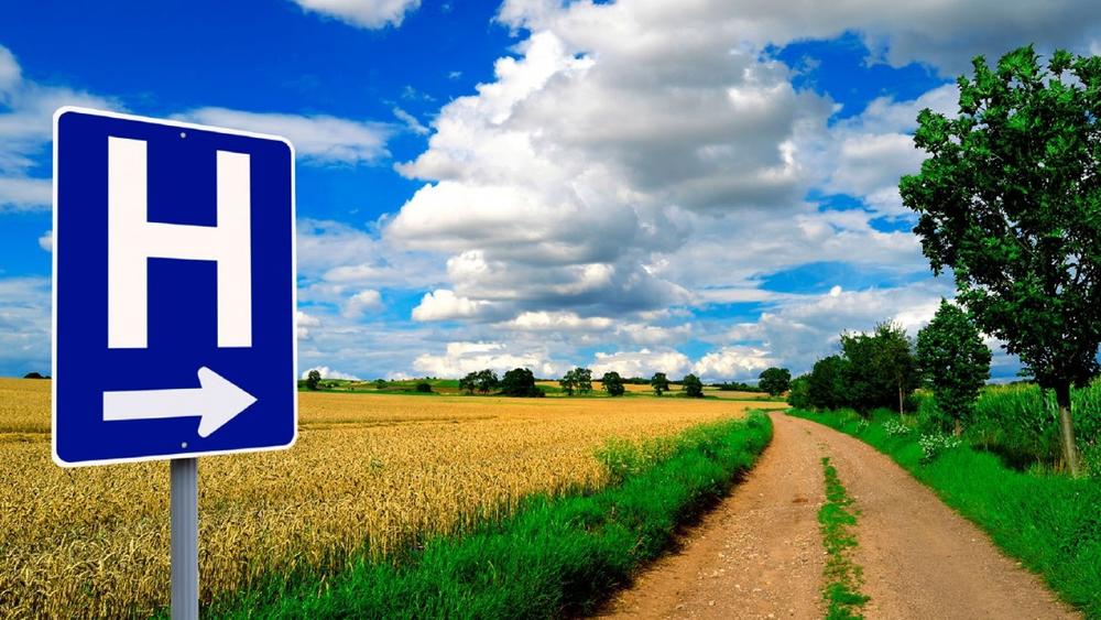 Blue and white hospital sign on dirt road