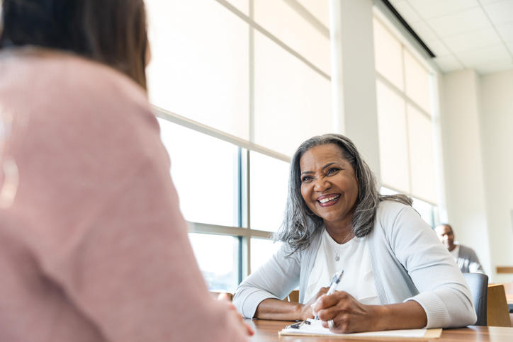 Woman sitting a table with pen and notepad smiling at another woman during an interview