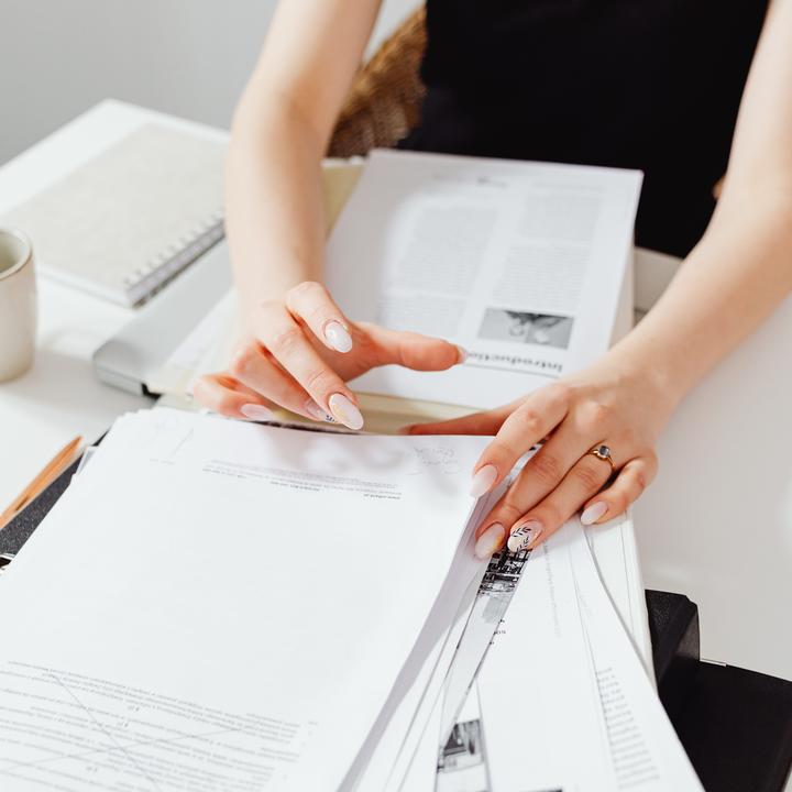 Woman's hands going through stacks of papers on a white desk.
