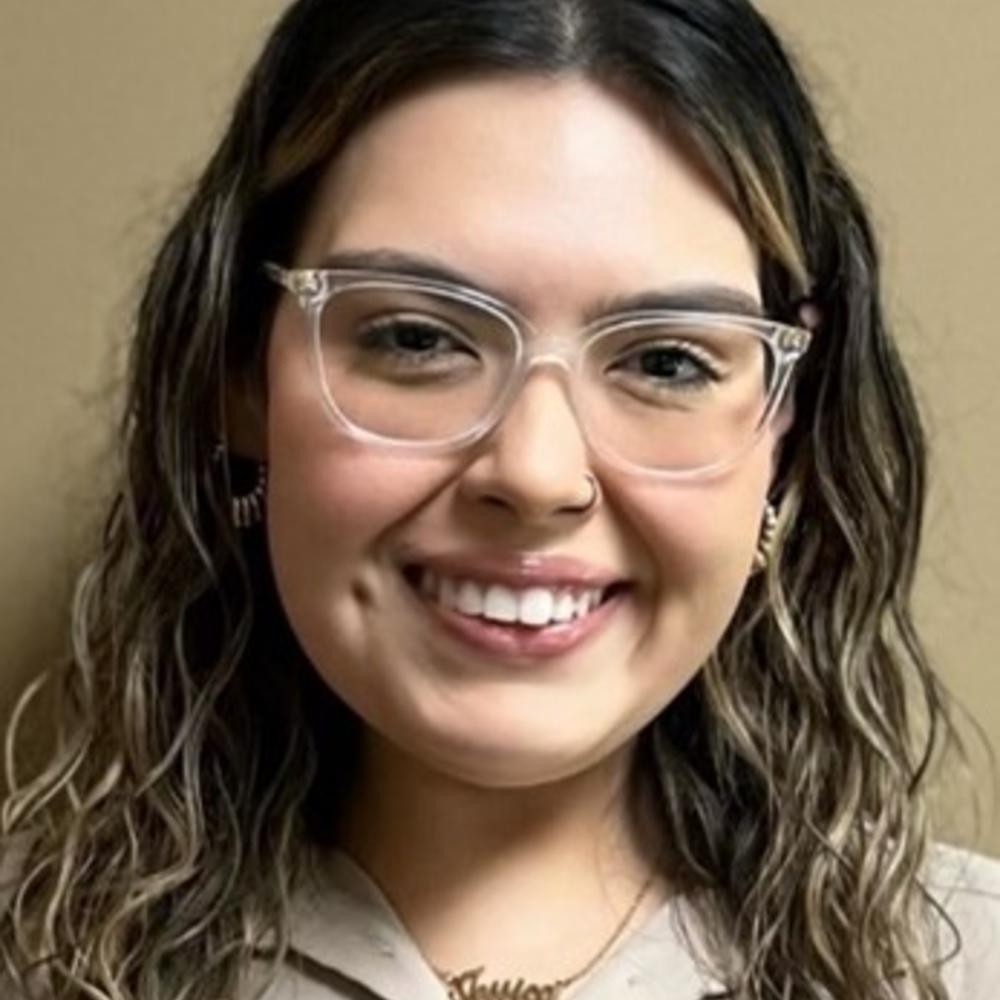 Headshot of female employee wearing glasses in front of tan background