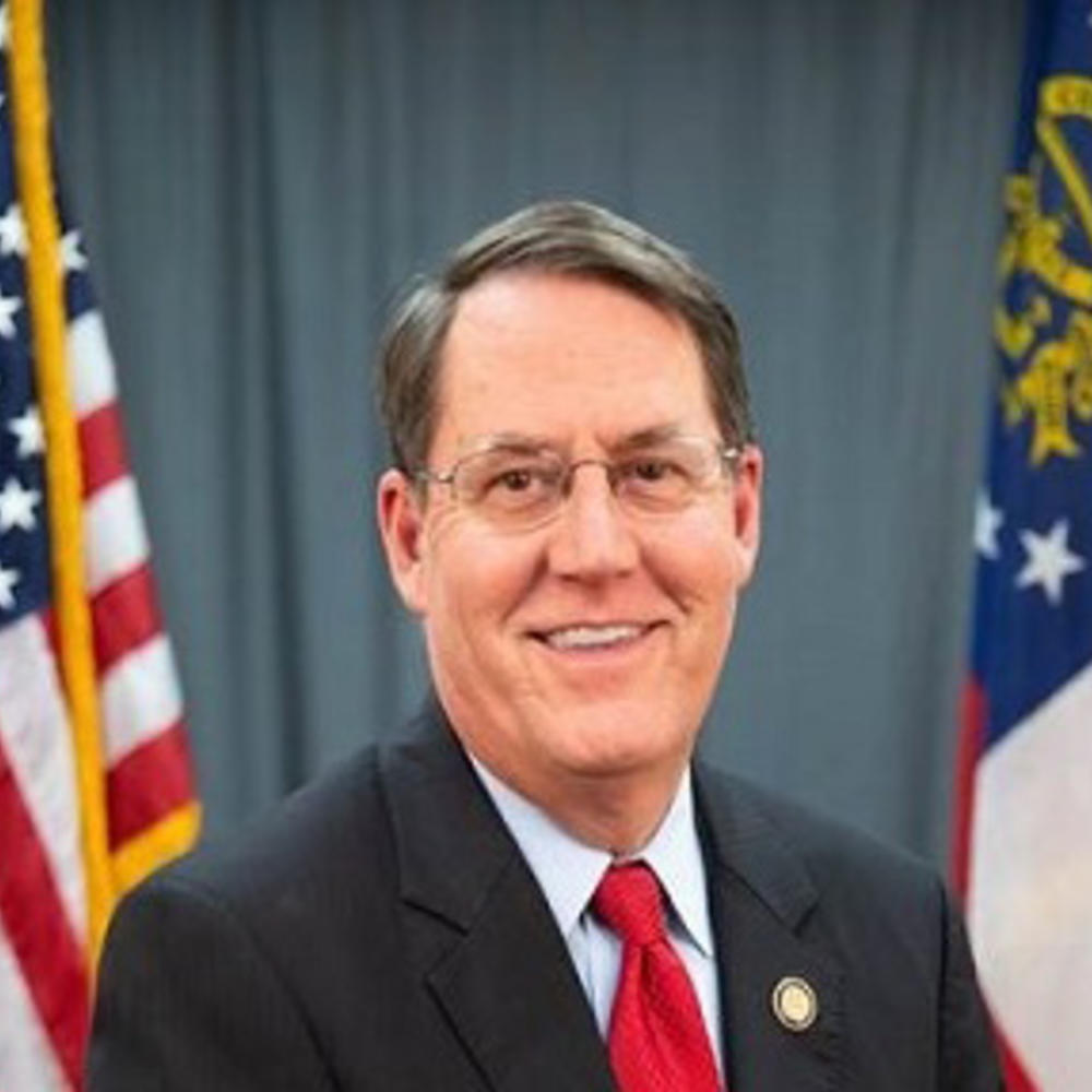 Headshot on gray background with American and Georgia flags