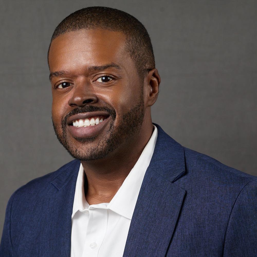 Headshot of male employee smiling in front of gray background 