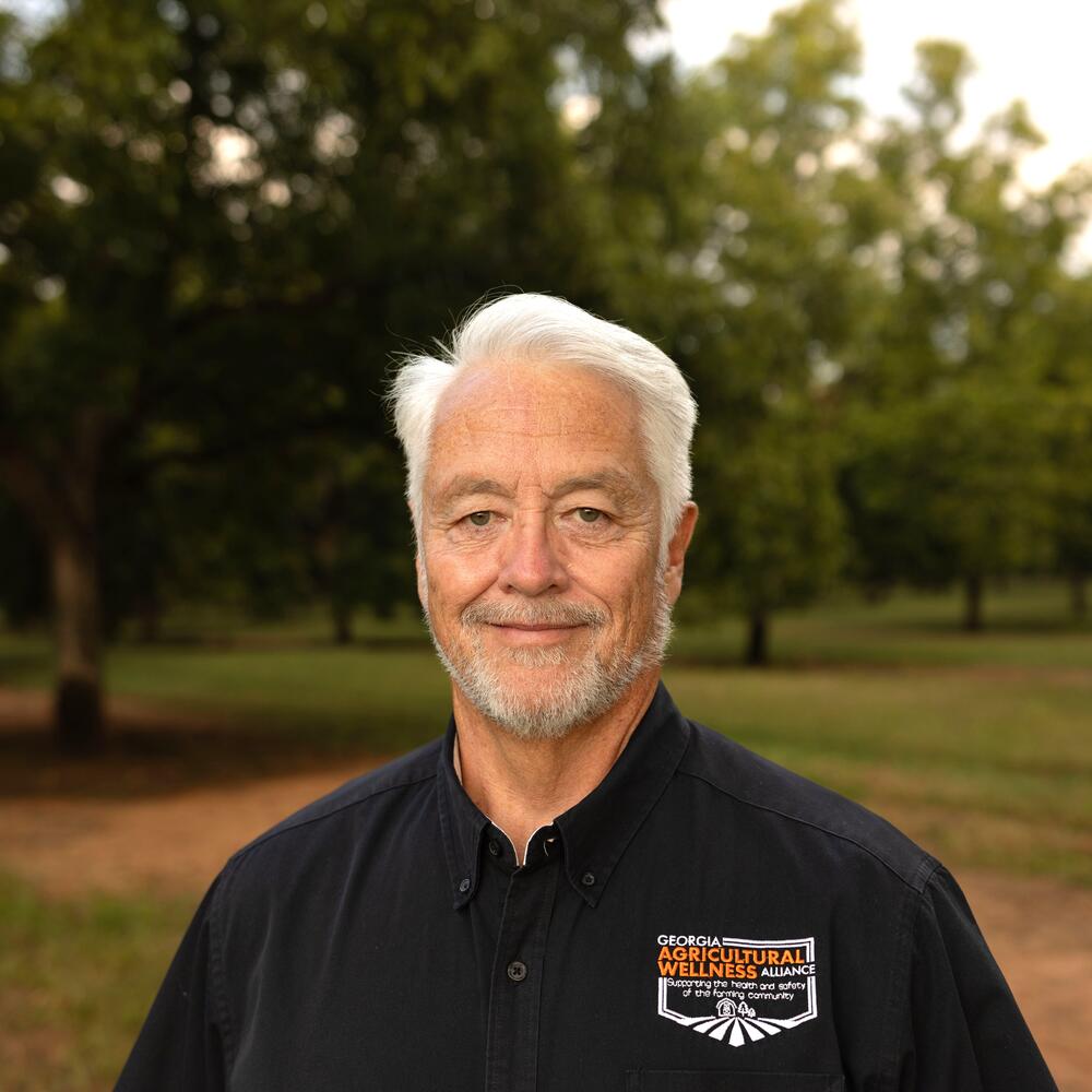 Photo of man smiling outside in field in front of trees