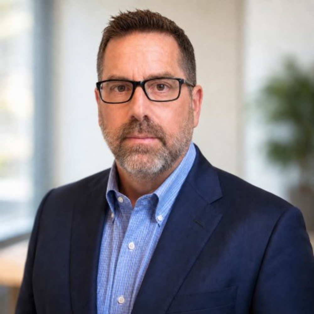 Headshot of man wearing glasses in front of a blurred office background 