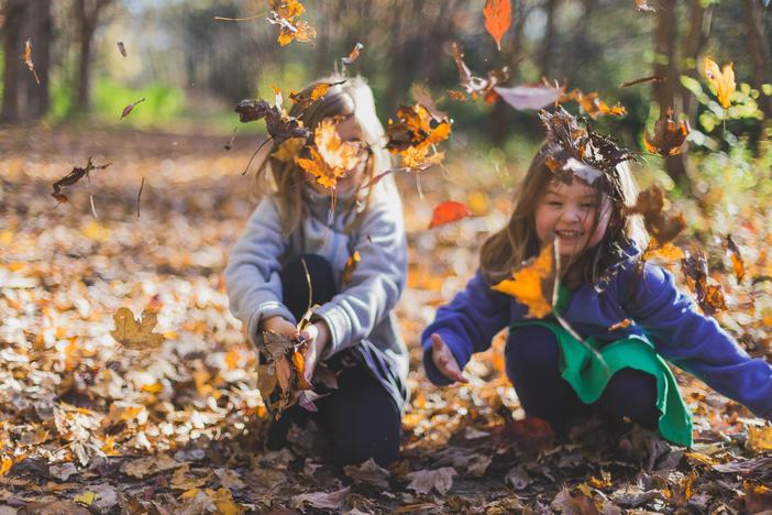 Two girls tossing fallen leaves in the air.