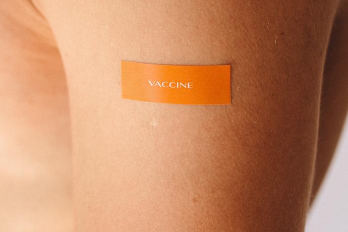 Closeup of orange bandage on an arm that says "vaccine."