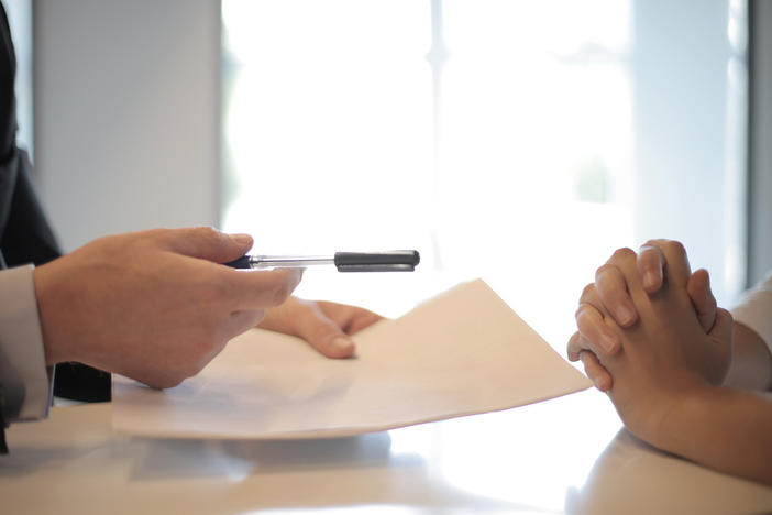 Up close image of a hands handing a piece of paper and a pen to another person's hands.
