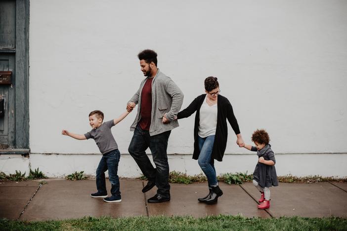 Family walking on sidewalk holding hands.